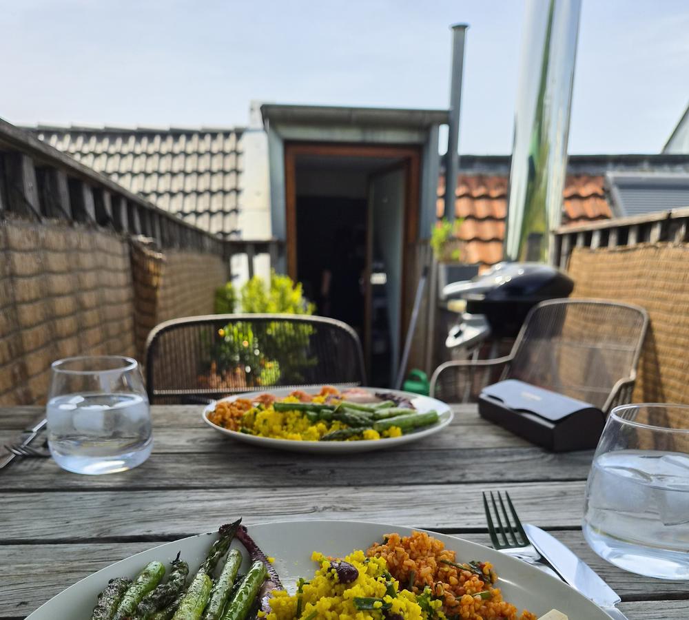 Gedeckter Tisch auf einer Dachterrasse mit Tellern, Gläsern und Grill