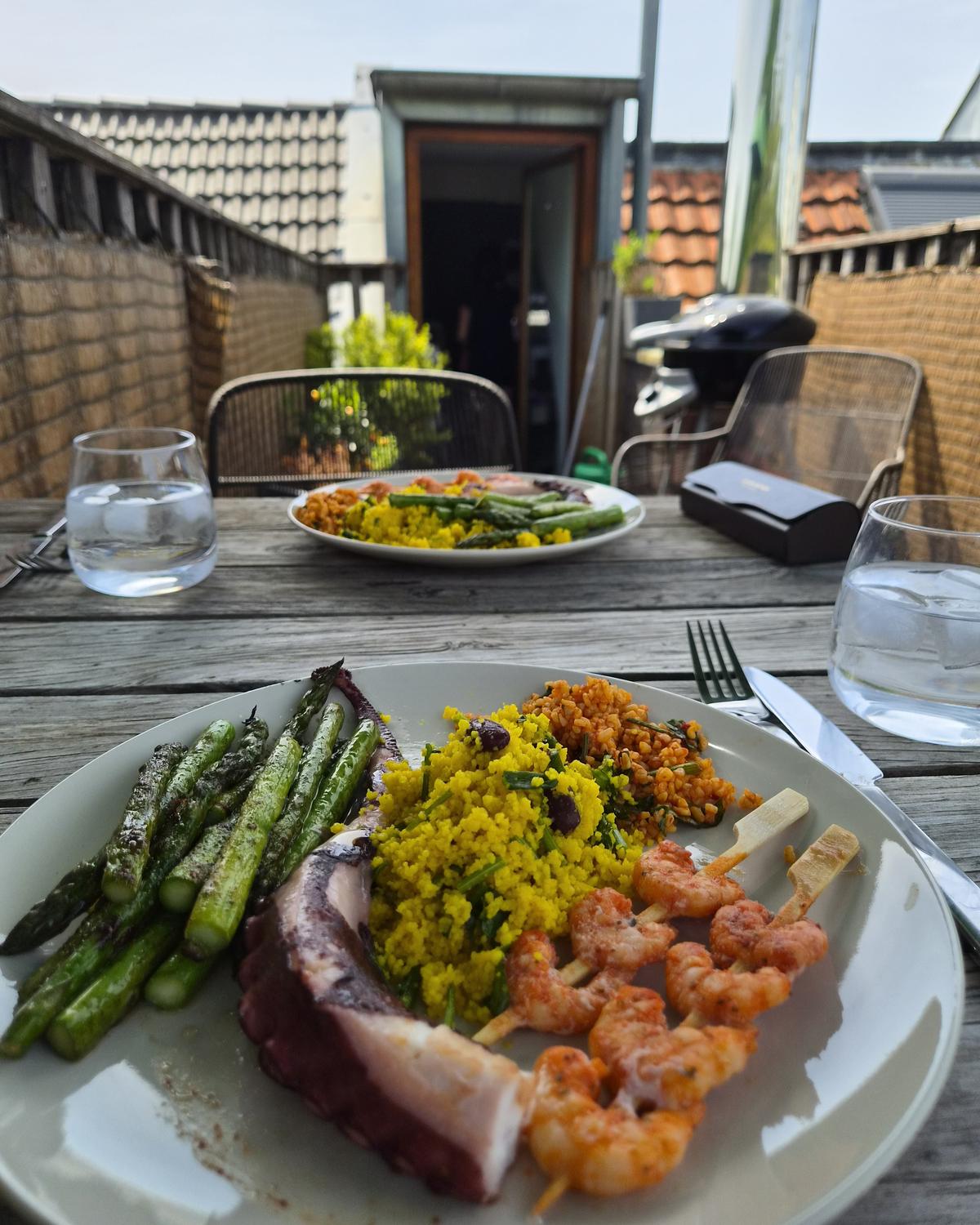 Gedeckter Tisch im Freien: Teller mit gegrilltem Spargel, Couscous, Bulgursalat und Garnelenspießen