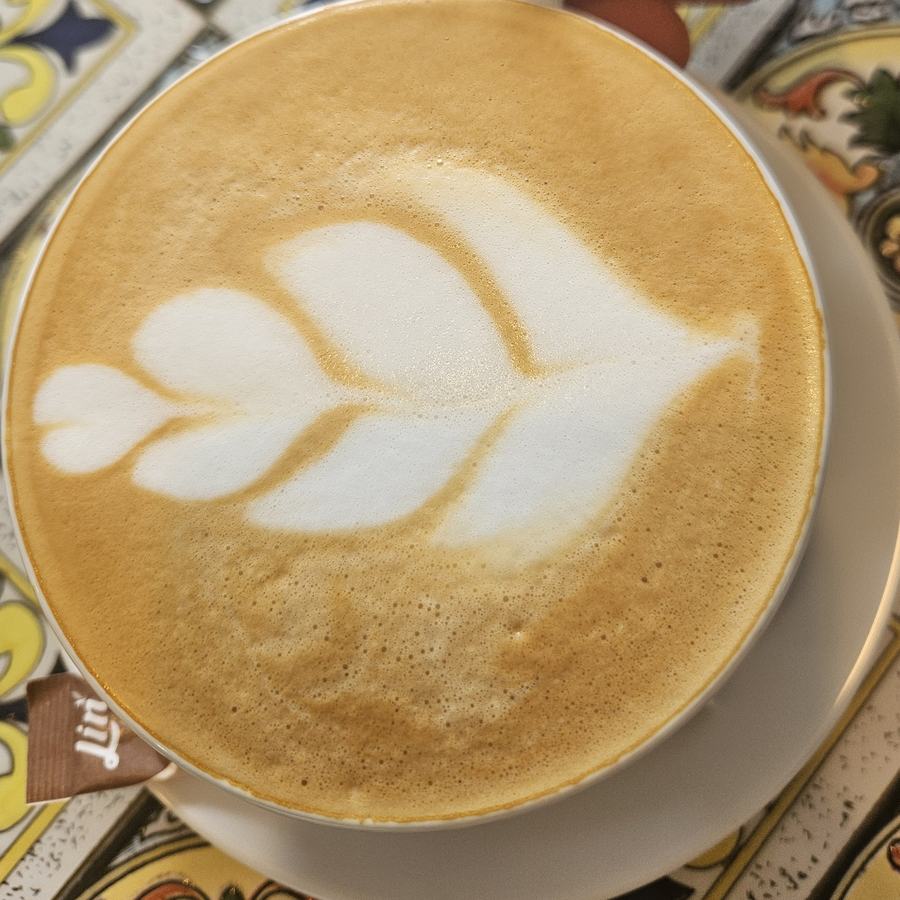 Tasse Cappuccino mit Milchschaummuster, daneben ein Zuckertütchen