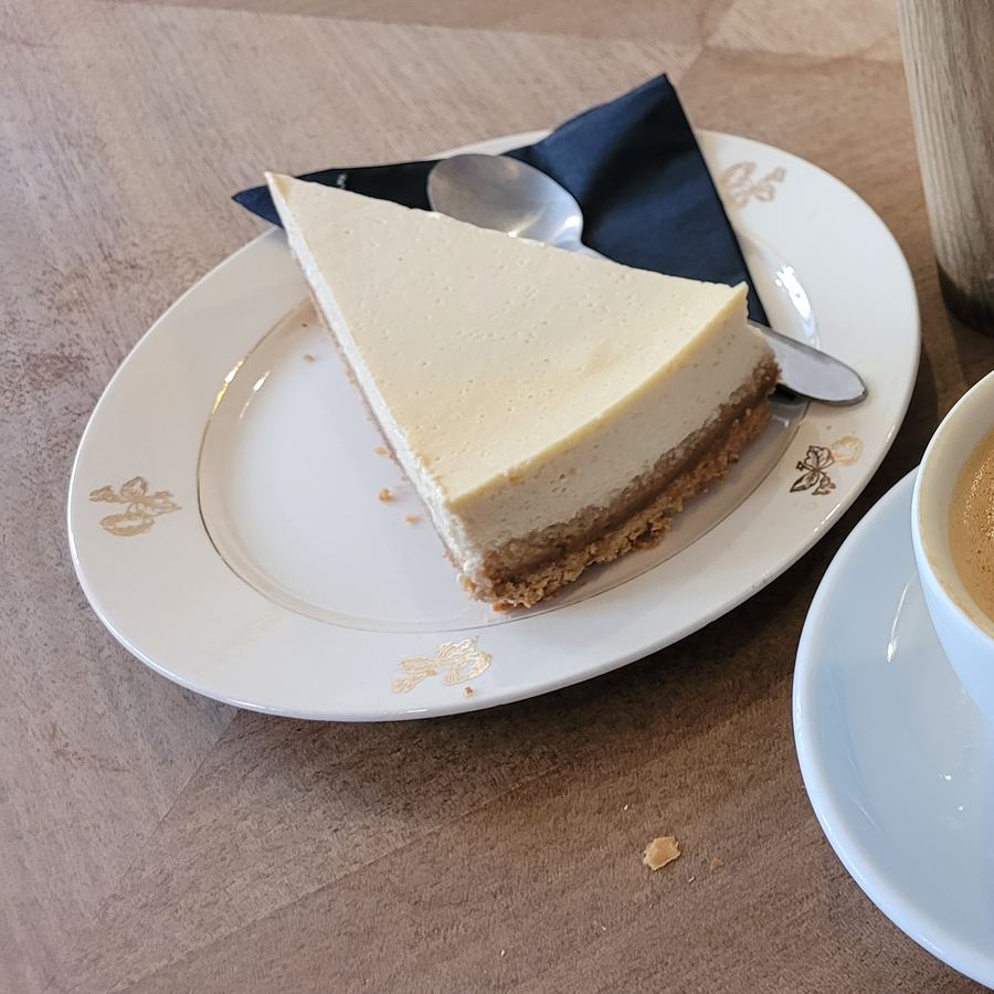 Stück Käsekuchen auf einem Teller neben einer Kaffeetasse