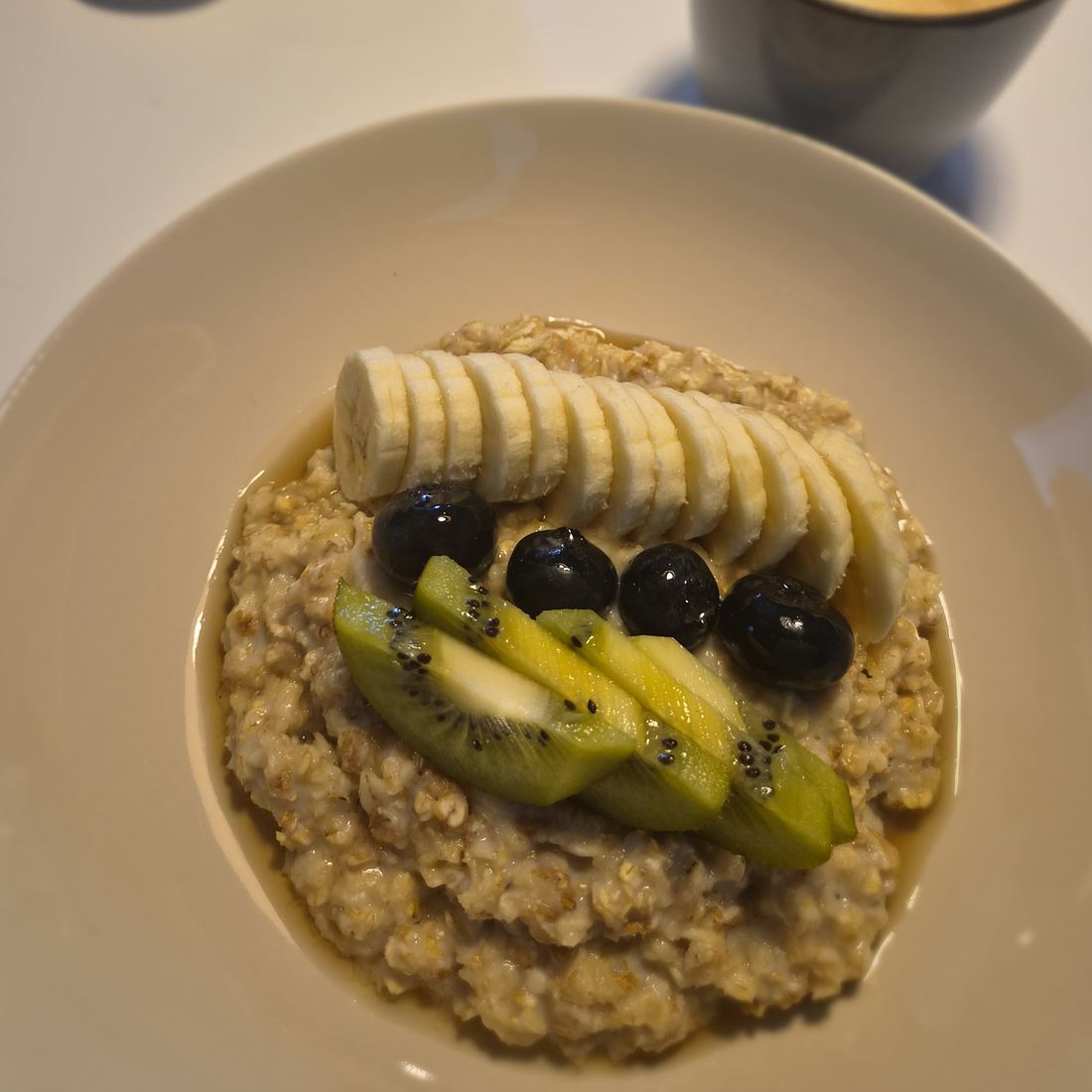 Schale mit Haferbrei, Bananenscheiben, Kiwi und Heidelbeeren von oben
